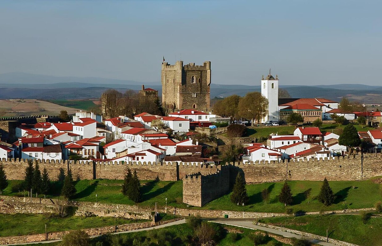 Imagem aréa da paisagem de Bragança, onde se vê o castelo, a moralha e vários edifícios, num dia com algumas núvens.