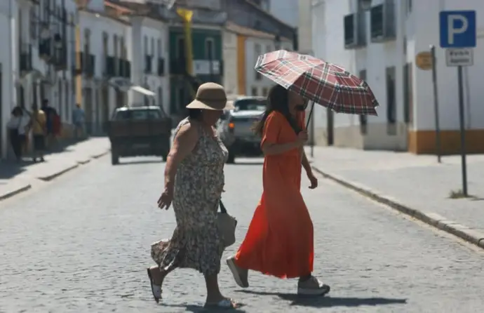 Duas senhoras com guarda sol caminham na rua