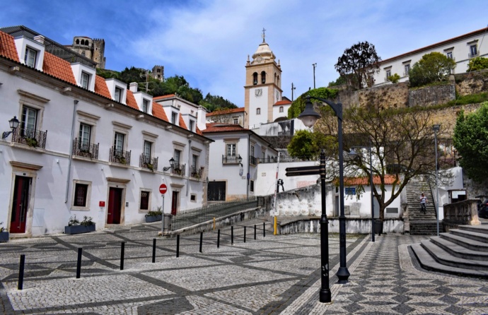 Uma rua da cidade de Leiria, onde estão alguns edifícios e a torre da igreja ao fundo, num dia limpo.