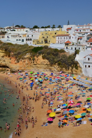 Praia de Carvoeiro, no Algarve cheia de pessoas, onde se vê a costa, com rochedos e casas num dia solarengo.