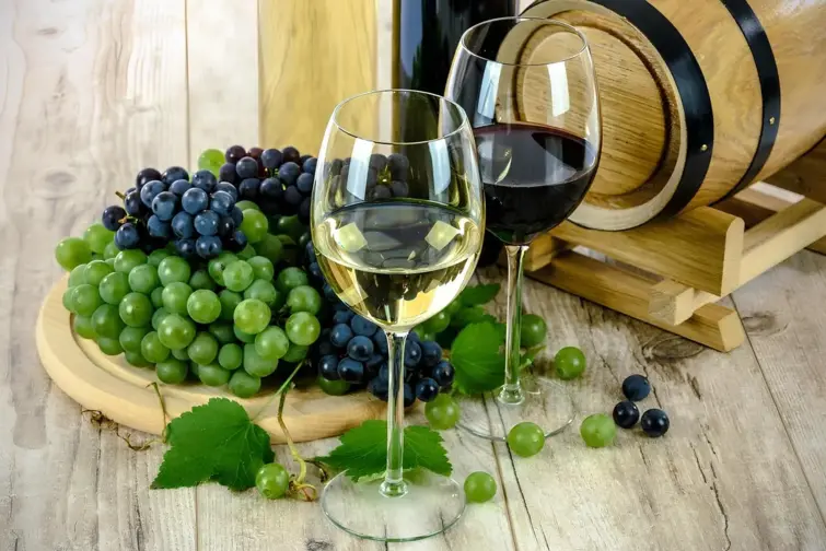 Dois copos de vinho, com uvas atrás e uma pequena pipa.