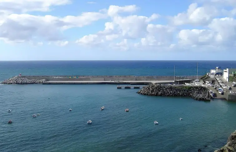 Porto de Rabo de Peixe, rodeado de mar, onde se vê rochedo e um edifício branco. 