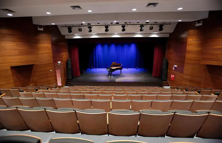 Um auditório em escada, visto do topo da plateia, com um piano em cima do palco.