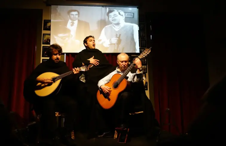 Fadista num palco, com dois guitarristas à frente, em Coimbra.