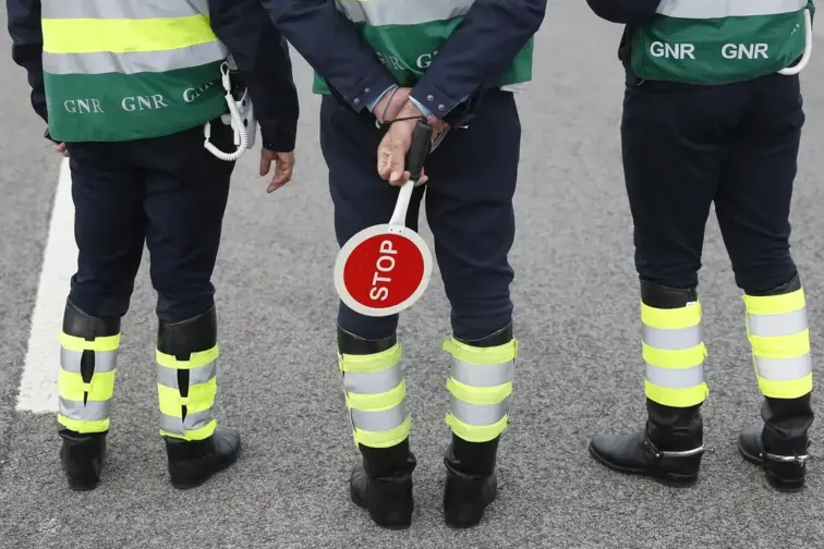 Três oficiais da GNR de costas numa estrada em plena operação. 
