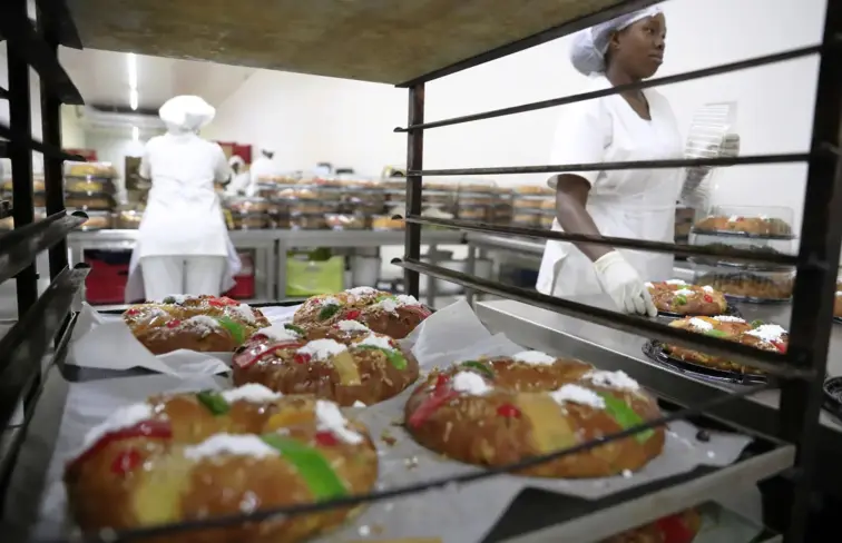 Cinco bolos-rei num tabuleiro, completamente confecionados, na zona de fazer bolos de uma padaria.