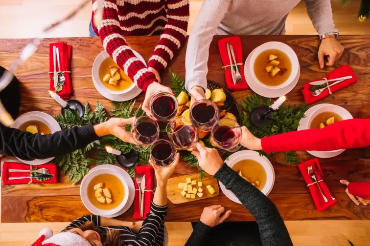 Mesa de Natal rodeada por seis pessoas a comerem e a brindarem com vinho