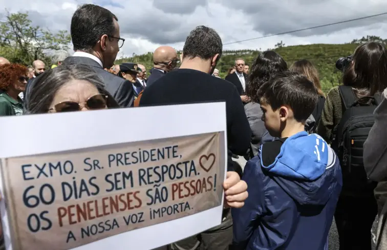 Pessoa levanta cartaz a pedir resposta aos atingidos pelas tempestades.