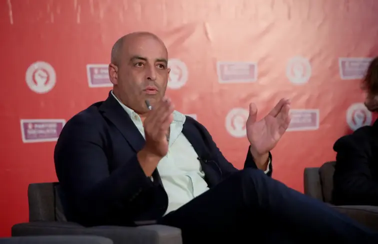 Ricardo Pinheiro, homem careca, sentado, a discursar, à frente de um placar do Partido Socialista.