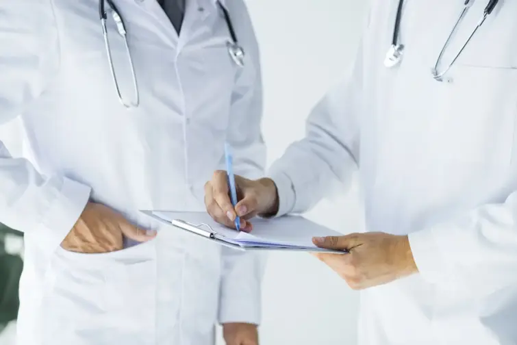 Dois médicos, vestidos de bata branca a analisar uns documentos