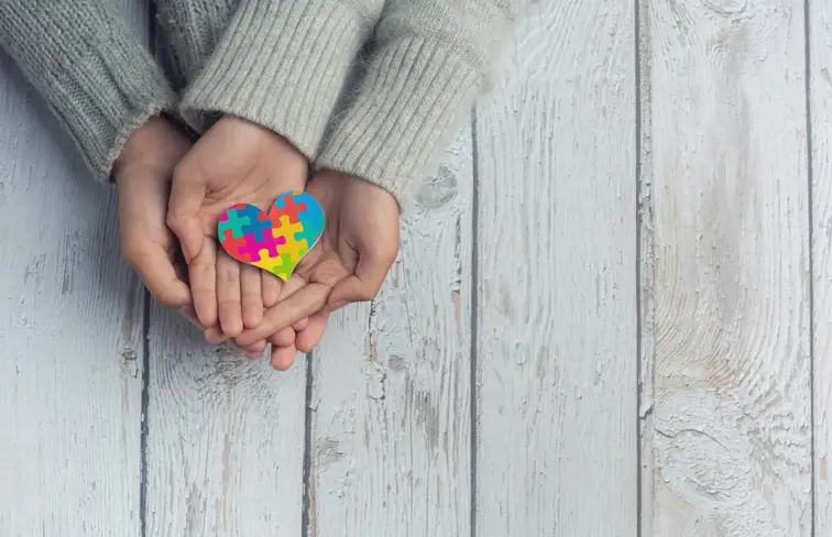 Mãos a segurar coração com símbolo de autismo