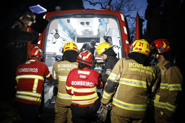 Bombeiros junto à porta de uma ambulância