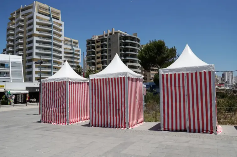 Barracas de praia listradas com edifícios atrás,