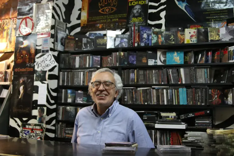 Miguel Teixeira, dono da loja Piranha, atrás do balcão com prateleiras de música atrás.