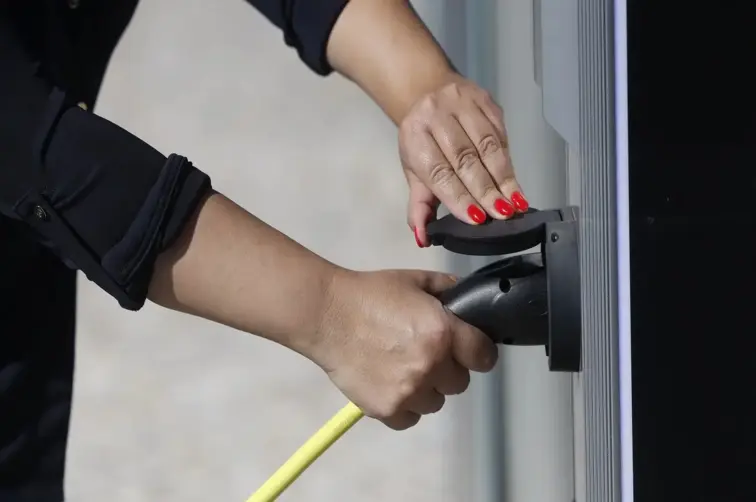 Mãos de uma pessoa a colocar viatura elétrica a carregar.