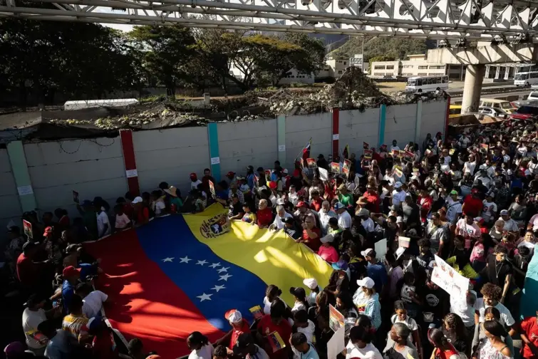 Multidão na rua com uma bandeira da Venezuela.