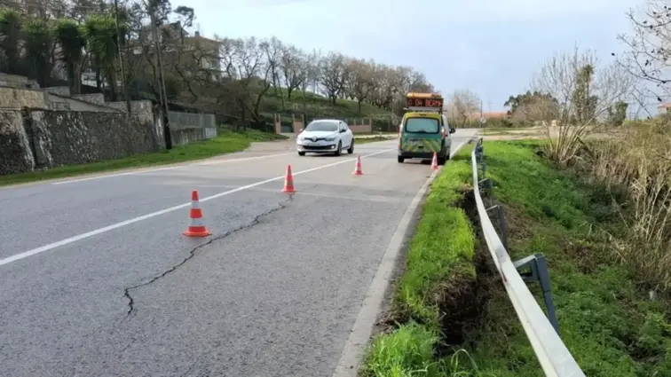 Estrada com estrago na berma junto a terreno.