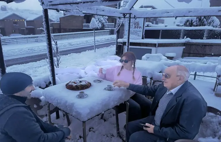 Três pessoas tomam café e bolo rei numa esplanada coberta de neve, em Castro Laboreiro