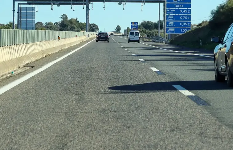 Carros na autoestrada. Ao fundo vê-se pórtico de portagens com indicação dos respetivos preços.