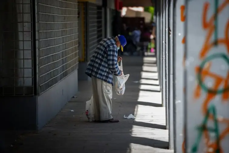 Na imagem, um homem idoso, de perfil, procura algo dentro de um saco de plástico.