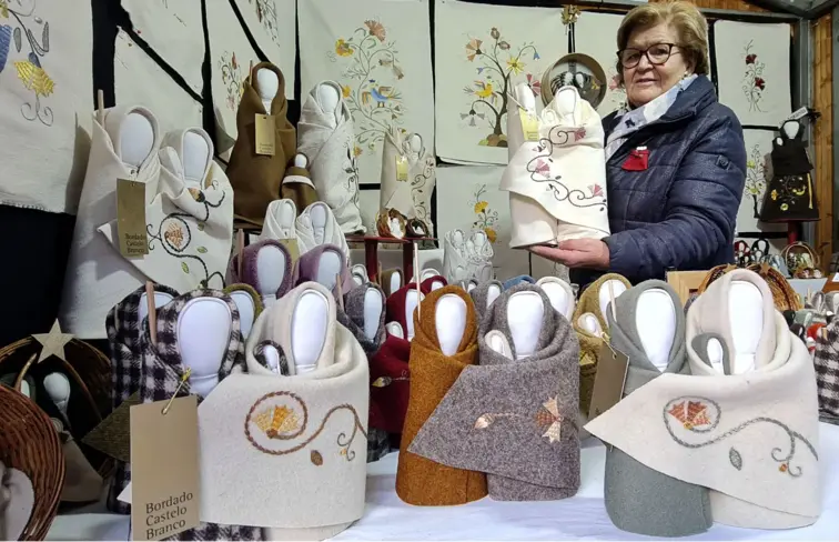 Mulher segura presépio feito com bordado de castelo branco e com outros em cima de uma banca