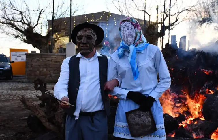 Duas pessoas mascaradas em festa tradicional transmontana. Ao fundo uma fogueira. 