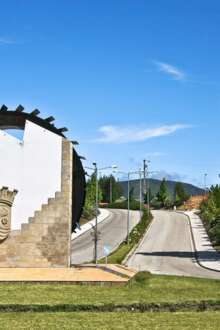 Brasão de Castanheira de Pera, numa parede em que a metade superior é branca e o restante é de pedra, num jardim. Atrás há duas estradas e árvores ao lado da estrada.