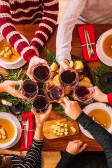 Mesa de Natal rodeada por seis pessoas a comerem e a brindarem com vinho