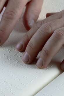 Mãos a tocar em papel em braille