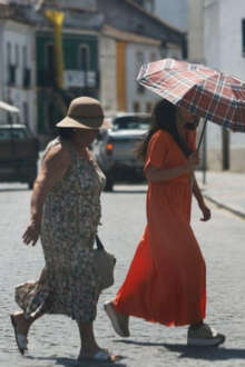 Duas pessoas a caminhar e a protegerem-se do calor com sombreiro