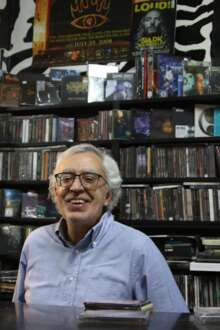 Miguel Teixeira, dono da loja Piranha, atrás do balcão com prateleiras de música atrás.